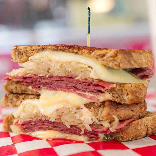 A stacked Reuben sandwich with corned beef, sauerkraut, and melted cheese on toasted rye bread.
