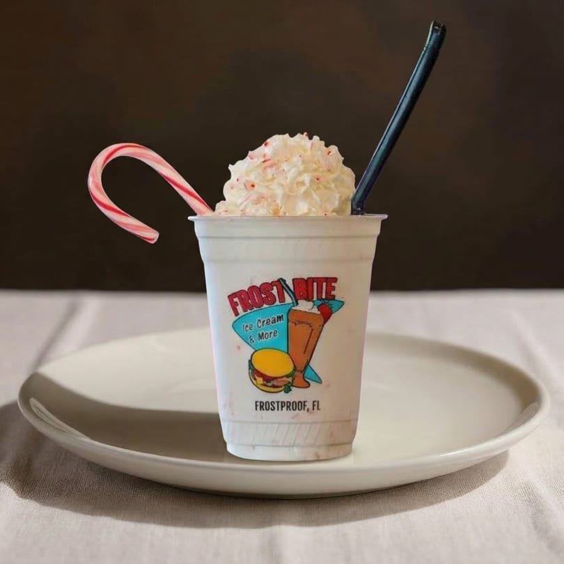A Frostbite Ice Cream & More milkshake with whipped cream, a candy cane, and a black straw.